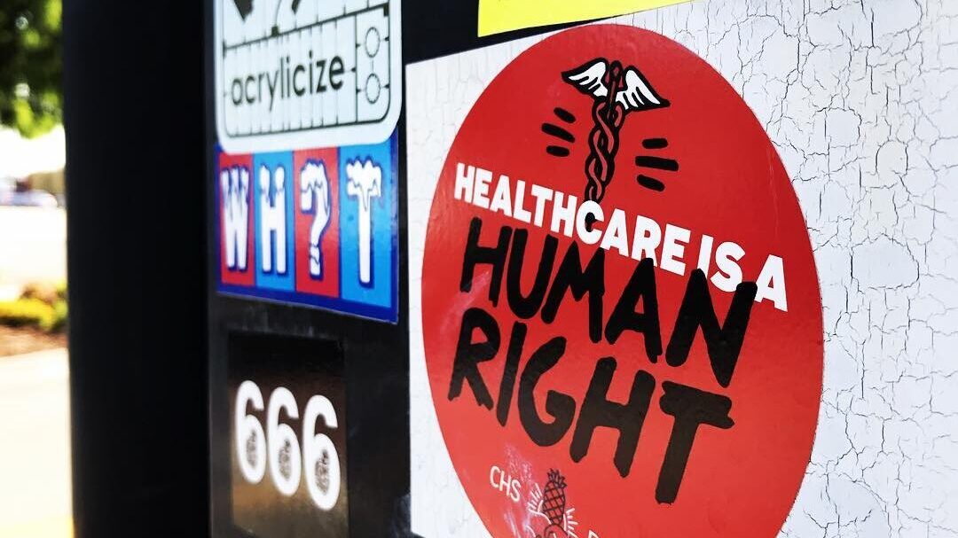 various sticker graffiti covers a surface.  one of the stickers reads "Healthcare is a Human Right"